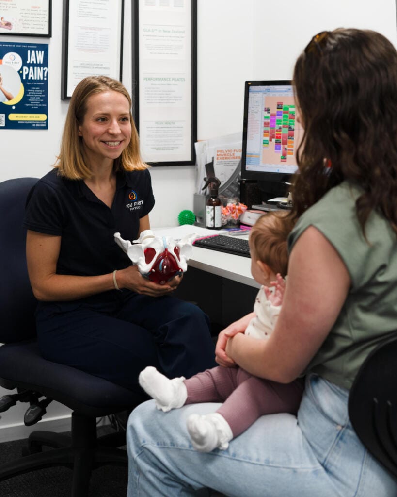 Physiotherapist explaining pelvic model to mother with baby