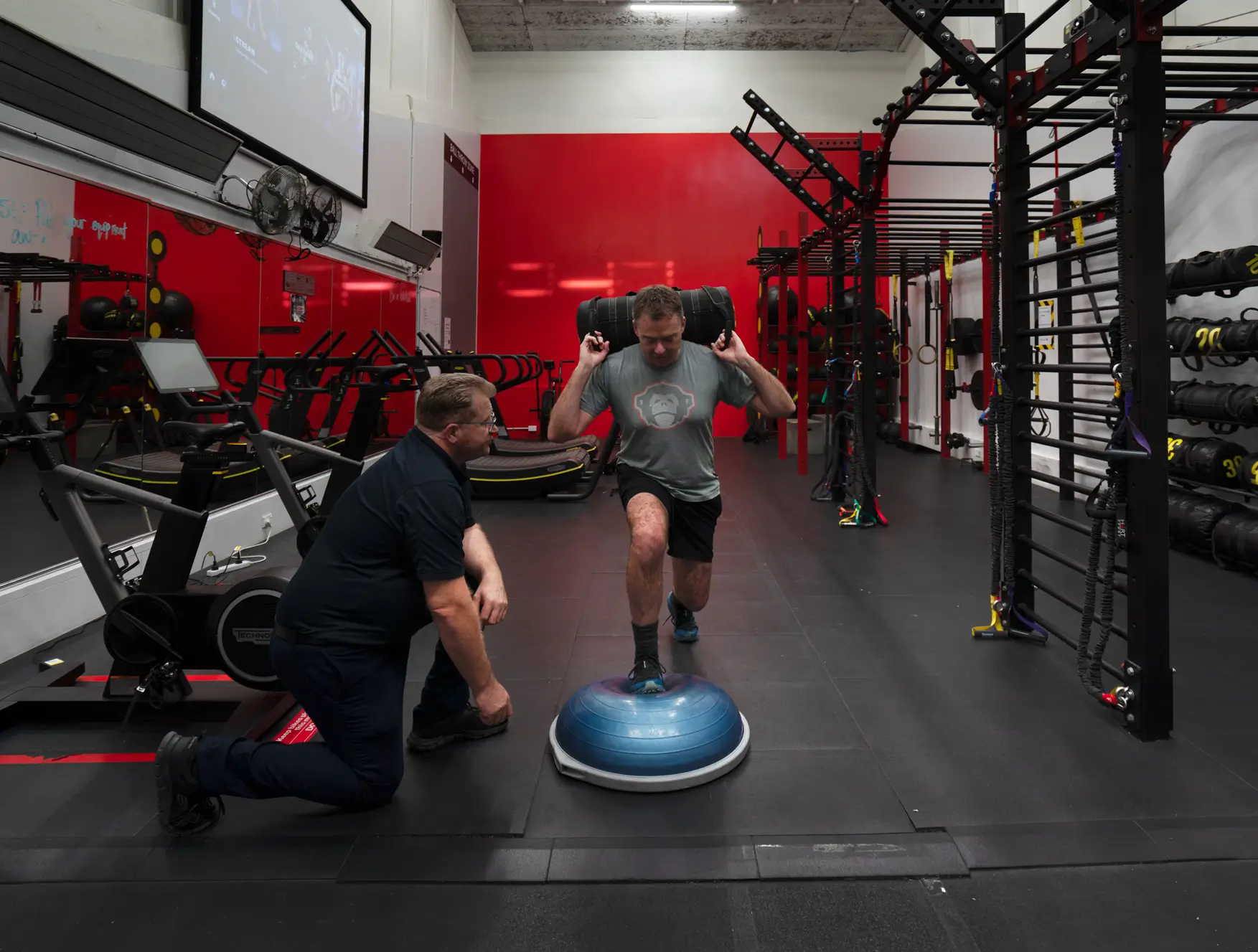 Man balancing on BOSU with trainer spotting