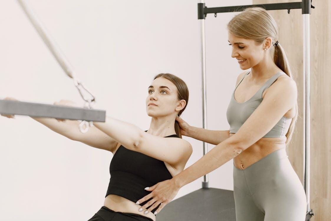Trainer assisting woman on Pilates reformer machine